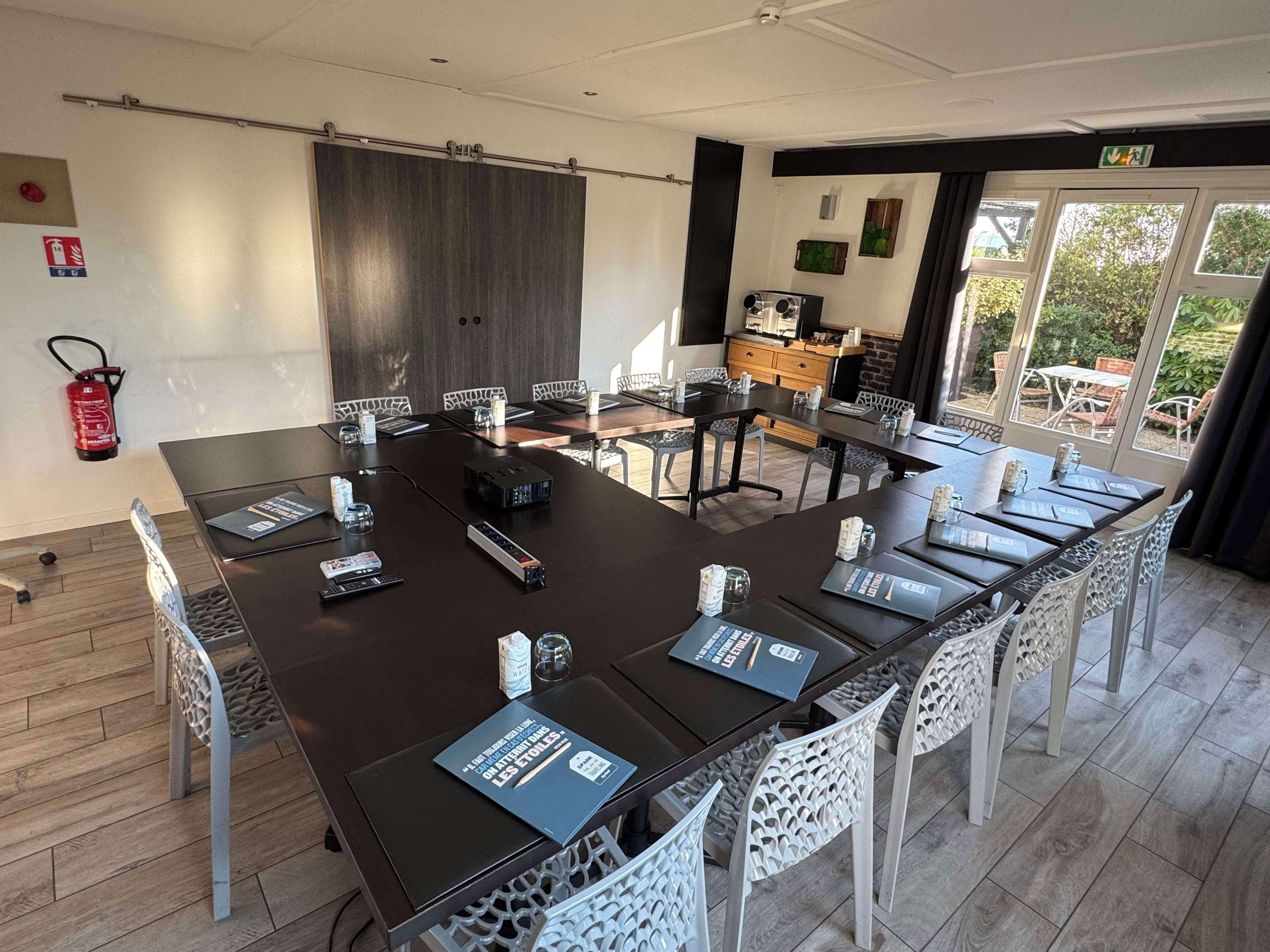 A conference room with a long table, white chairs, and a fire extinguisher on the wall.