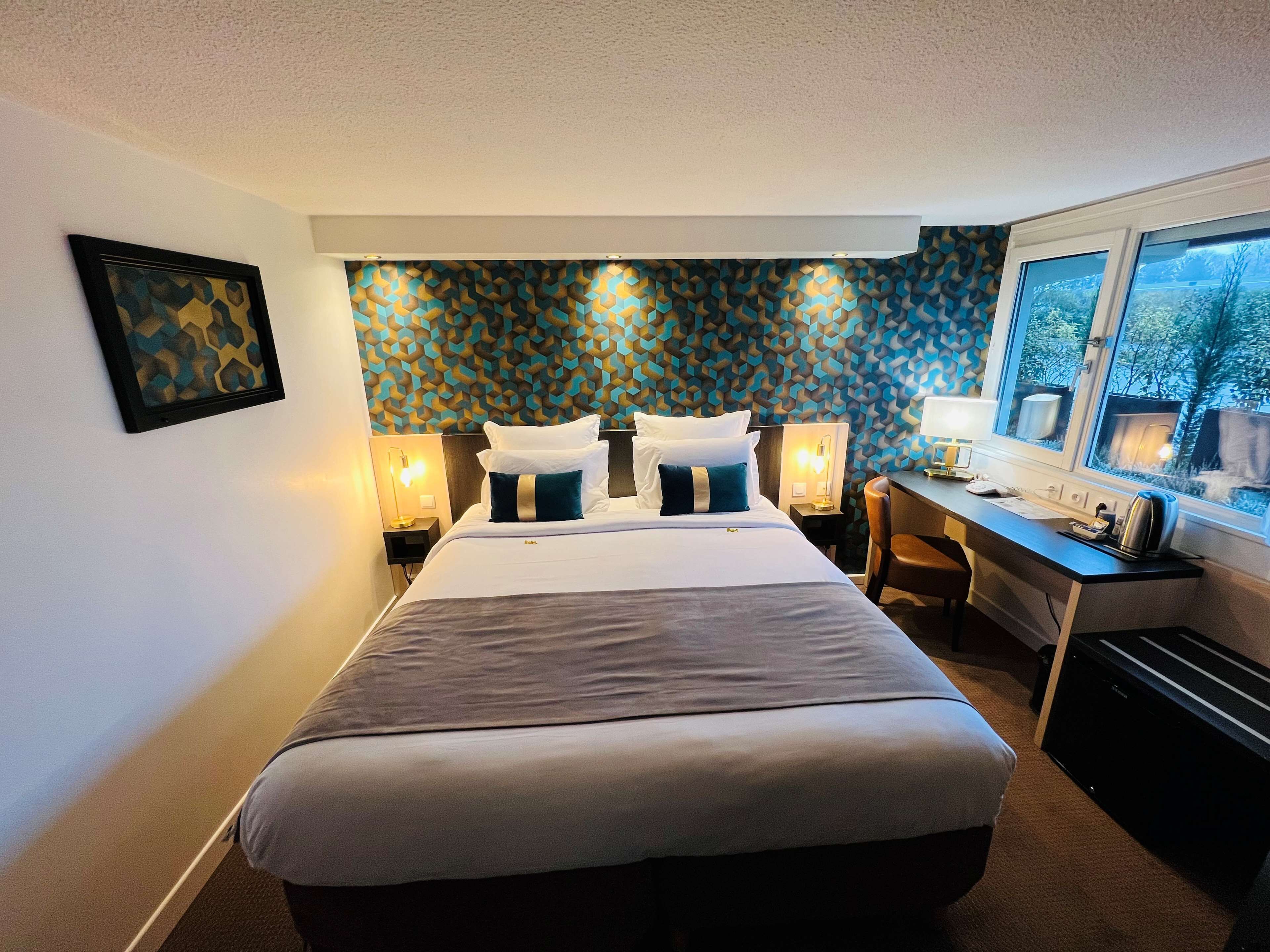 A hotel room with a bed, bedside tables, a desk, and a window with a view.