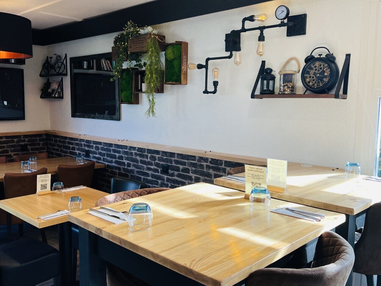Interior de restaurante com mesas e cadeiras de madeira, e parede de tijolos decorativa.