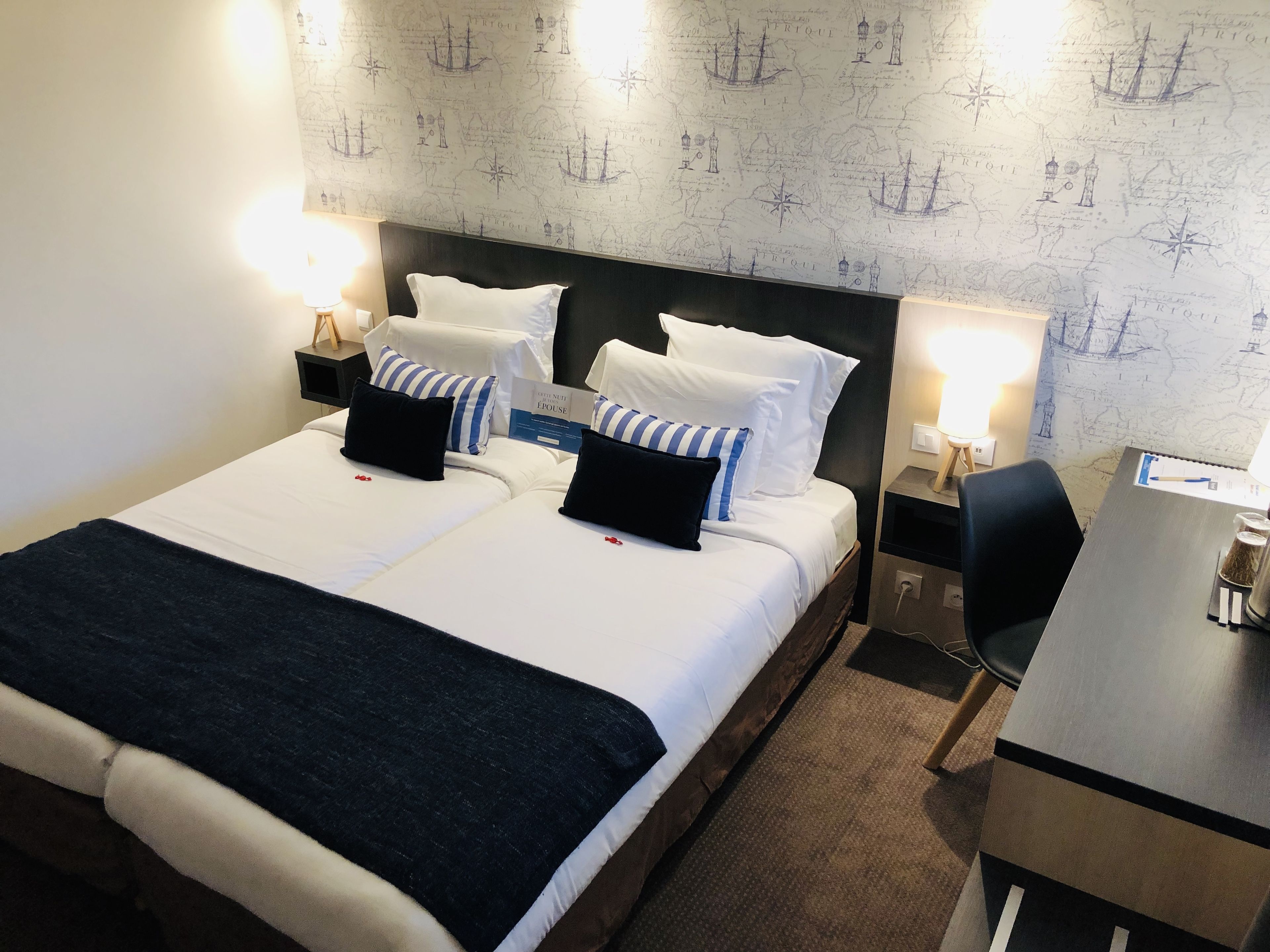 A hotel room with a large bed, two bedside tables, a desk, and a map-themed wall.