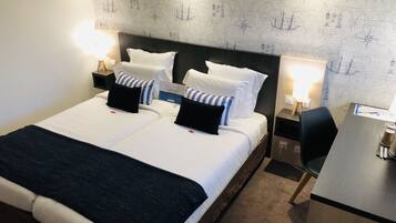 A hotel room with a large bed, two bedside tables, a desk, and a map-themed wall.