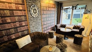 A cozy reading area with a leather sofa, a round wooden table, and a bookshelf filled with books. - Kyriad Lisieux (Lisieux)