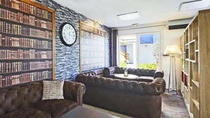 A cozy reading area with leather sofas, a coffee table, and a wall of bookshelves. - Kyriad Lisieux (Lisieux)