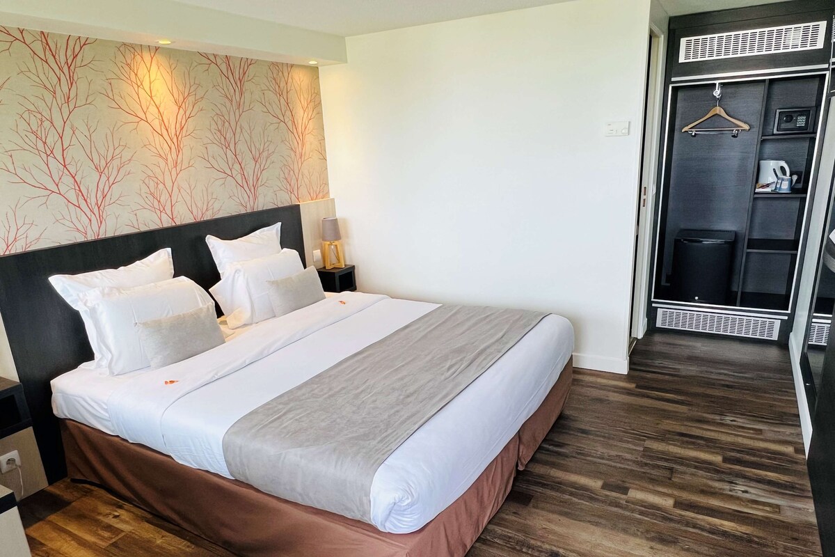 A neatly made bed with white and grey linens, a dark headboard, and a wooden floor.