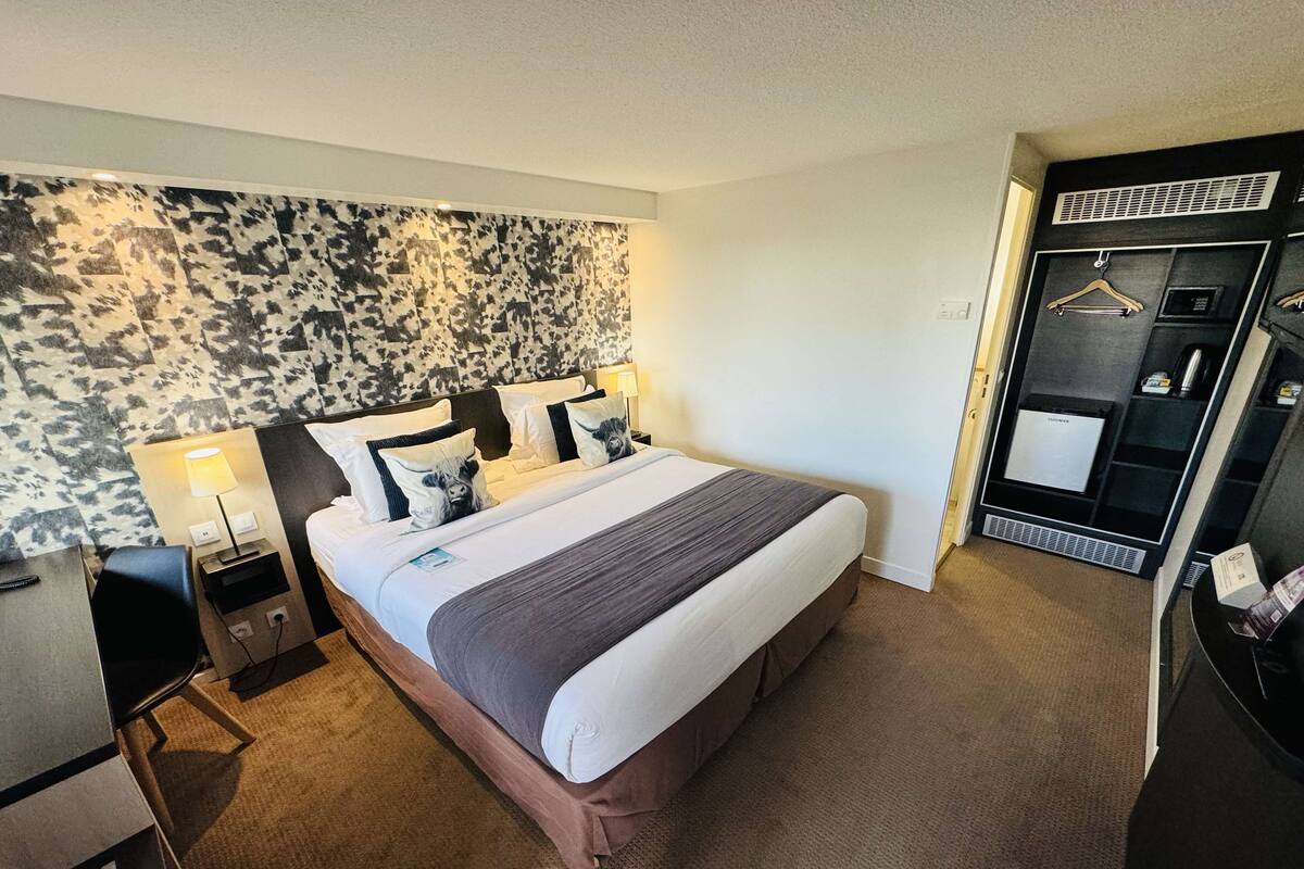 A hotel room with a bed, bedside tables, a lamp, a wardrobe, and a mirror.
