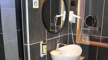 Un baño moderno con un lavamanos blanco, paredes con azulejos oscuros y una encimera de madera.