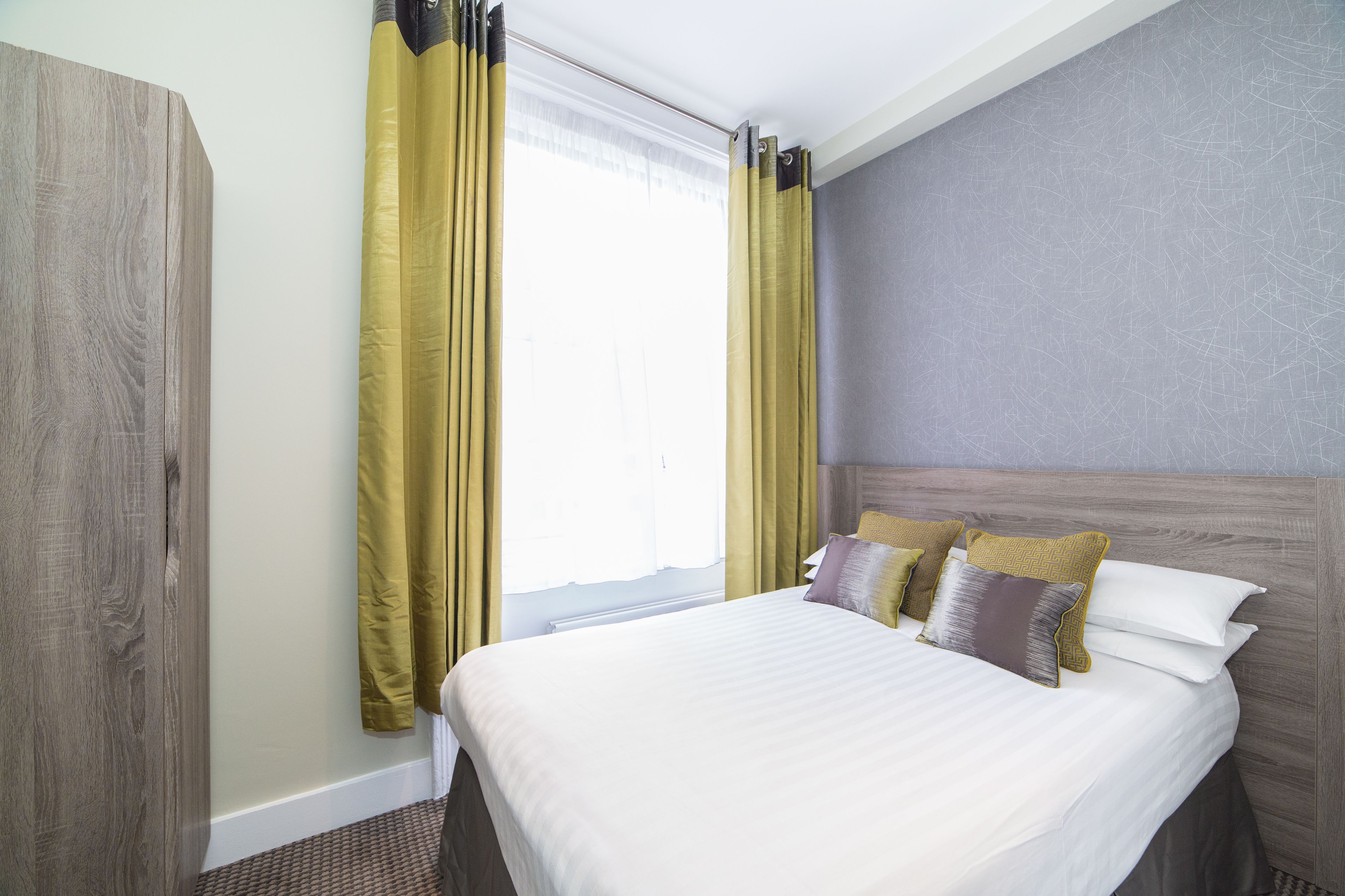 A hotel room with a bed, curtains, and a headboard.