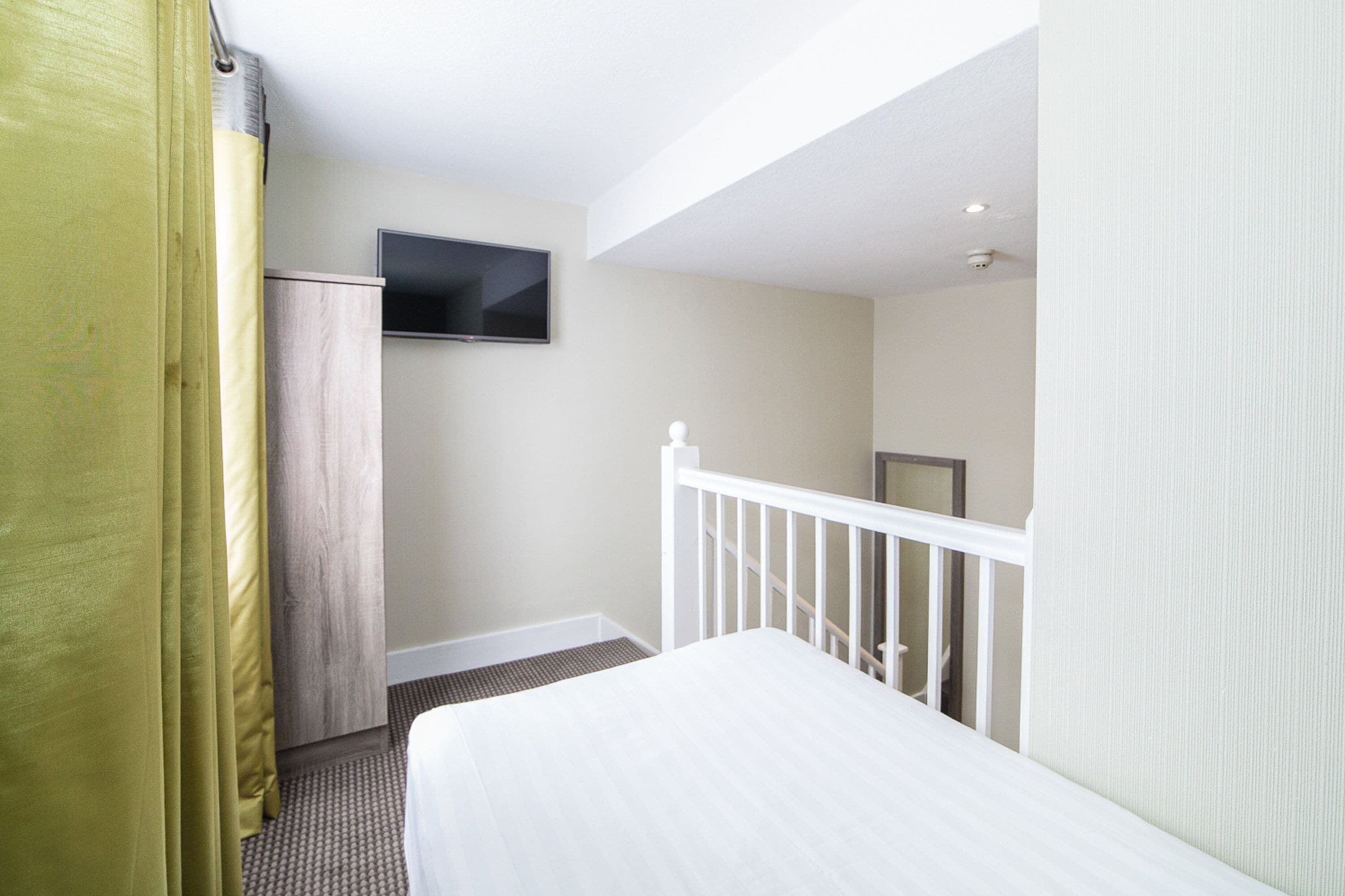 A hotel room with a bed, a television mounted on the wall, and a staircase leading to another room.
