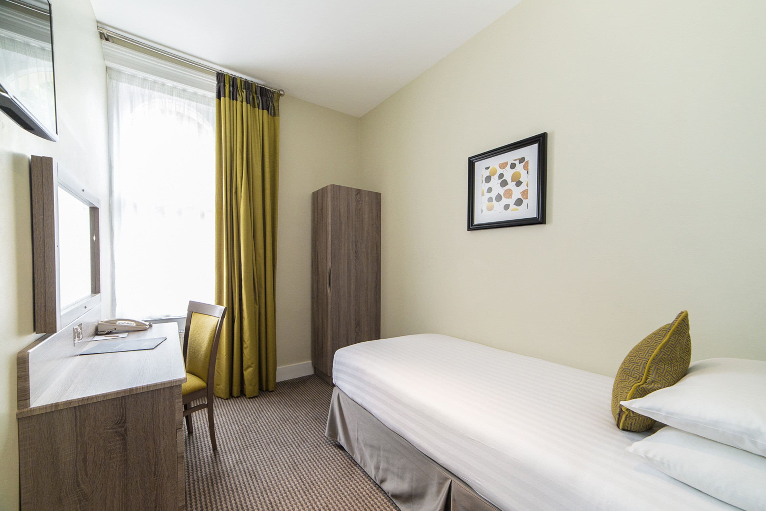 Ein Hotelzimmer mit Bett, Schreibtisch, Stuhl, Kleiderschrank und einem gerahmten Bild an der Wand.