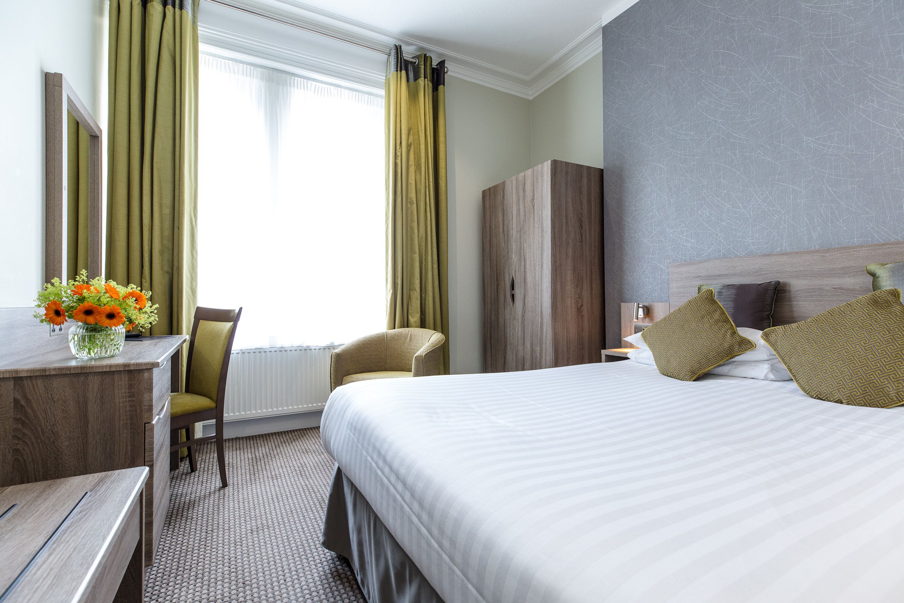 Una habitación de hotel con una cama grande, un escritorio con un florero, una silla y un armario.