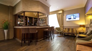 A bar area with stools, a television screen, and a seating area with a sofa and chairs. - Phoenix Hotel (London)
