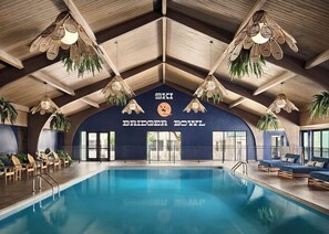 An indoor swimming pool with lounge chairs and a ceiling with wooden beams and hanging lights.