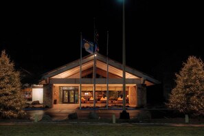 A building with a stone facade, a flagpole with a flag, and a well-lit entrance.