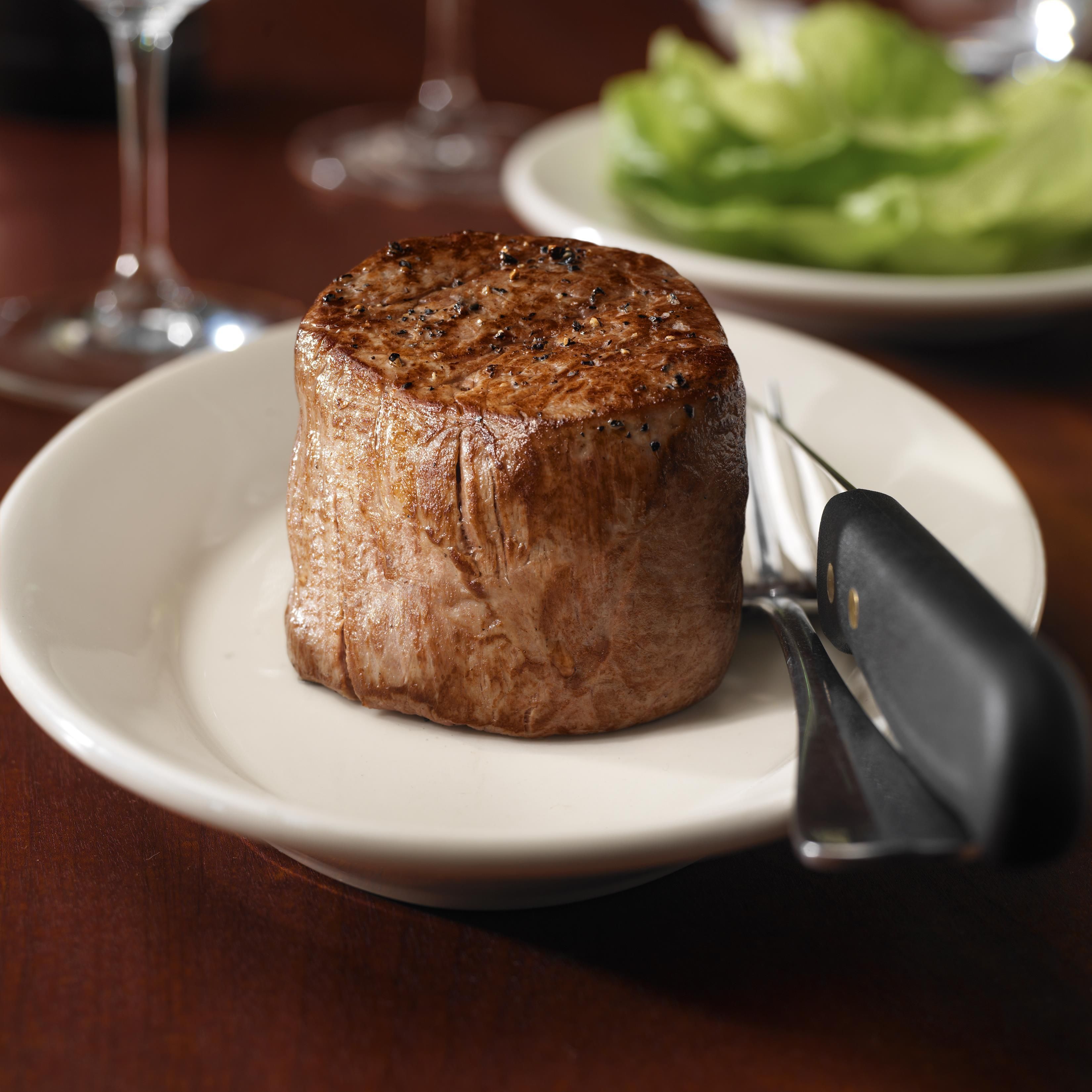 A steak on a plate with a knife beside it.