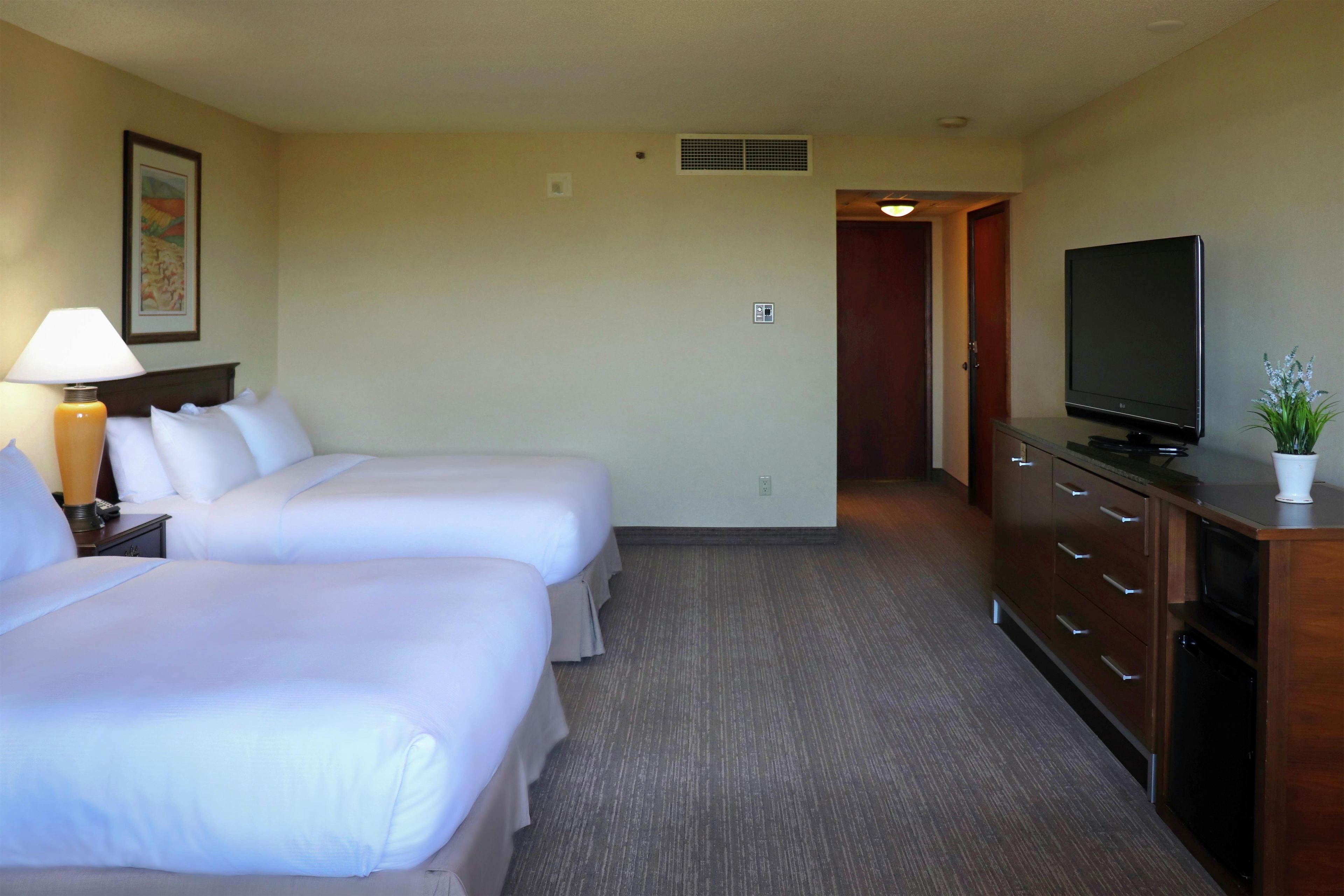 Habitación de hotel con dos camas, un televisor, un aparador y un pasillo que conduce a otra habitación.