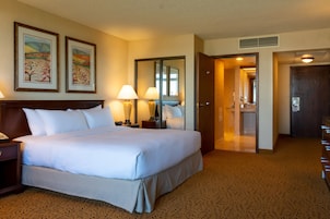 Habitación de hotel con una cama grande, dos lámparas de noche, una mesita de noche, un aparador, un espejo y dos cuadros en la pared.