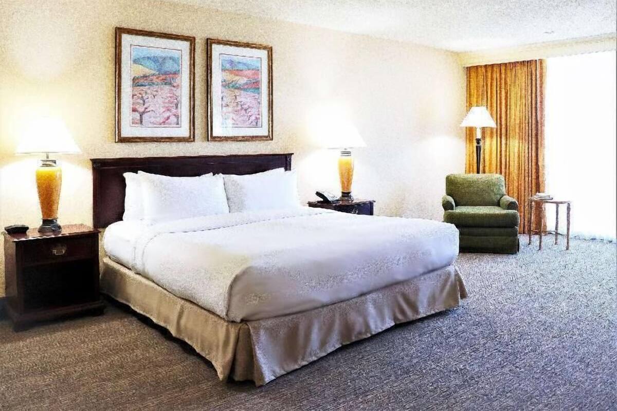 A hotel room with a bed, two nightstands, a chair, and two framed pictures on the wall.