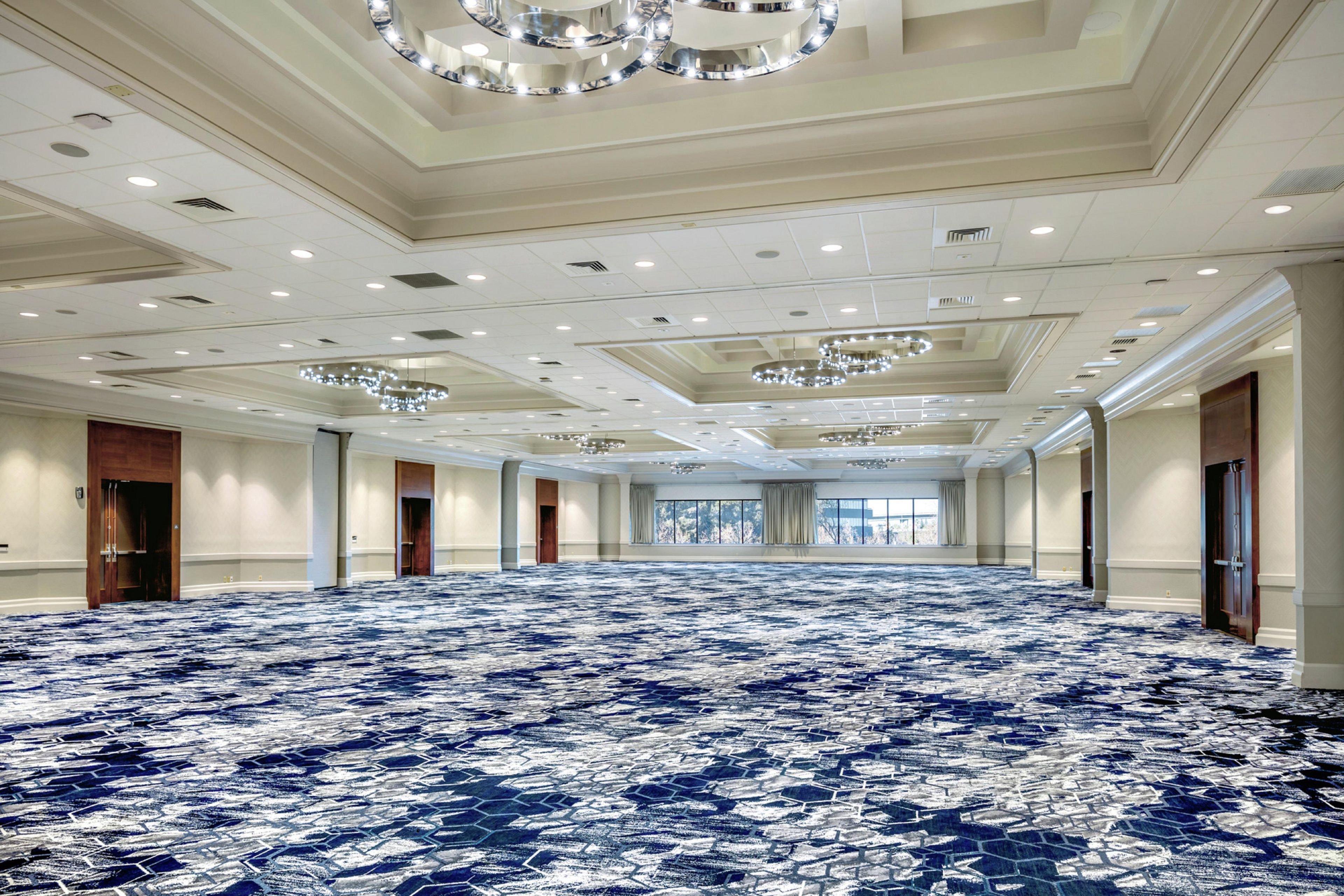 A large, empty hotel room with a patterned carpet, recessed lighting, and a chandelier.