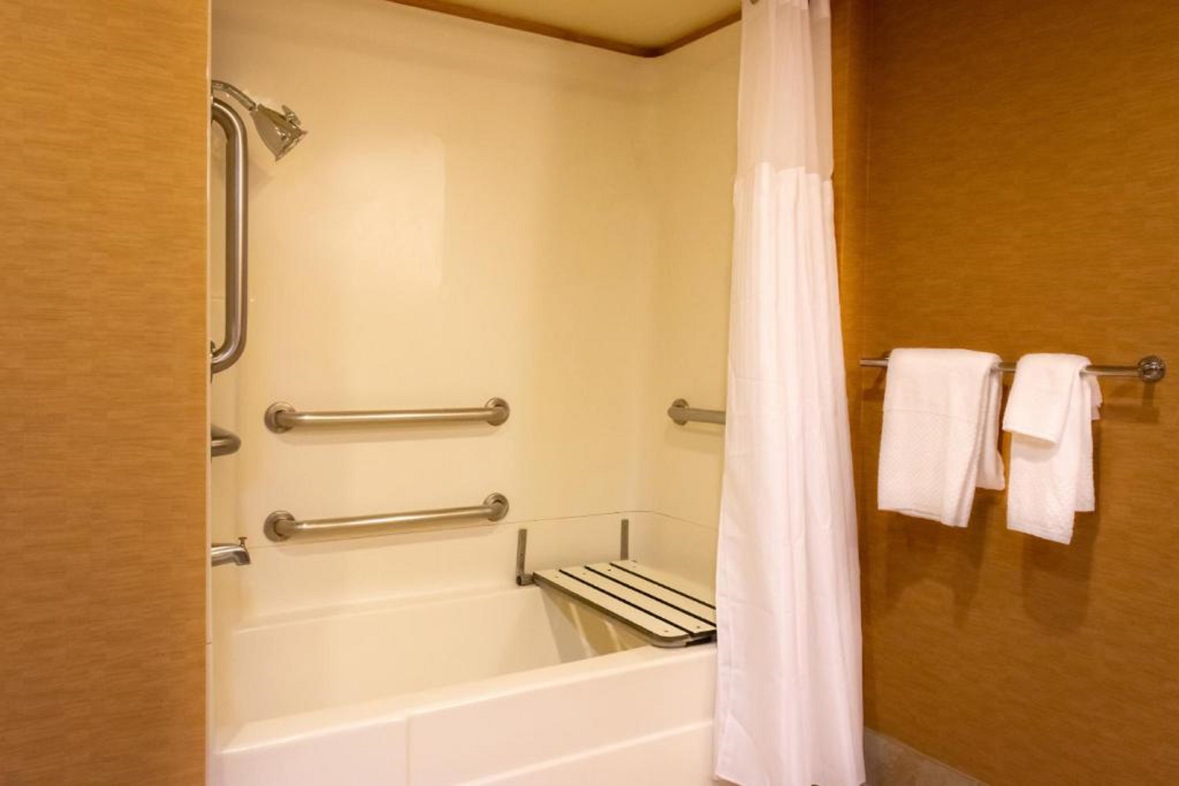 A bathroom with a bathtub, grab bars, a towel rack, and a shower curtain.