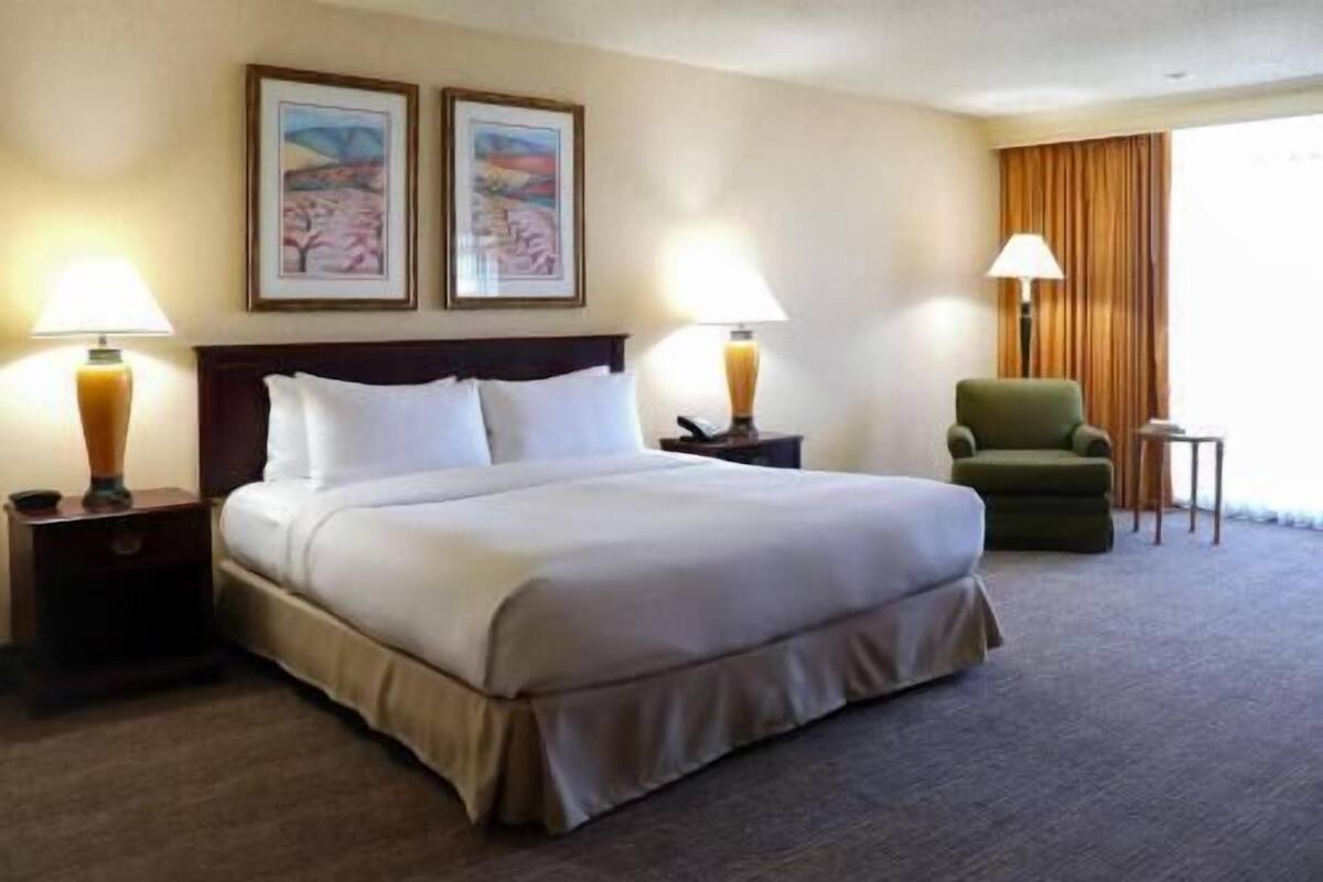 A hotel room with a bed, two lamps, a chair, and two framed pictures on the wall.