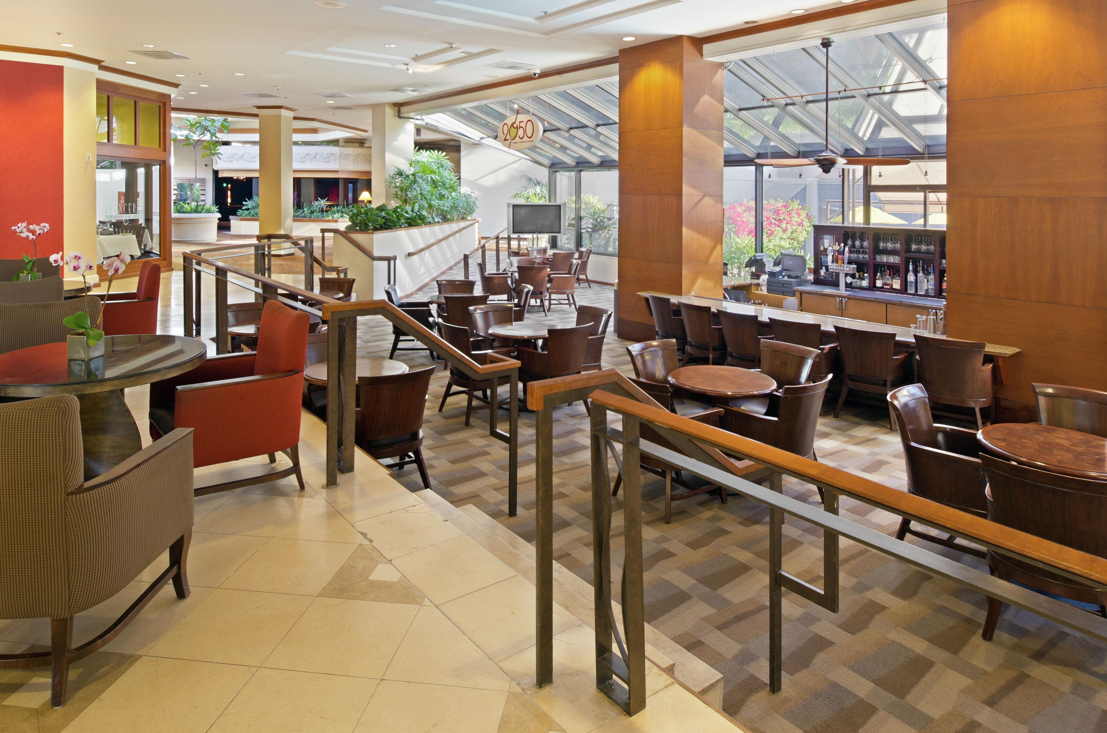 Eine großzügige Hotelhalle mit mehreren Sitzbereichen, einer Bar und einer Treppe zu einer oberen Ebene.