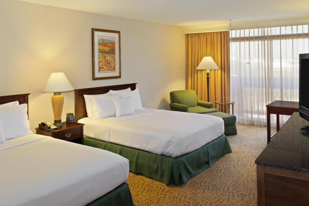 A hotel room with two beds, a television, a lamp, a chair, and a painting on the wall.