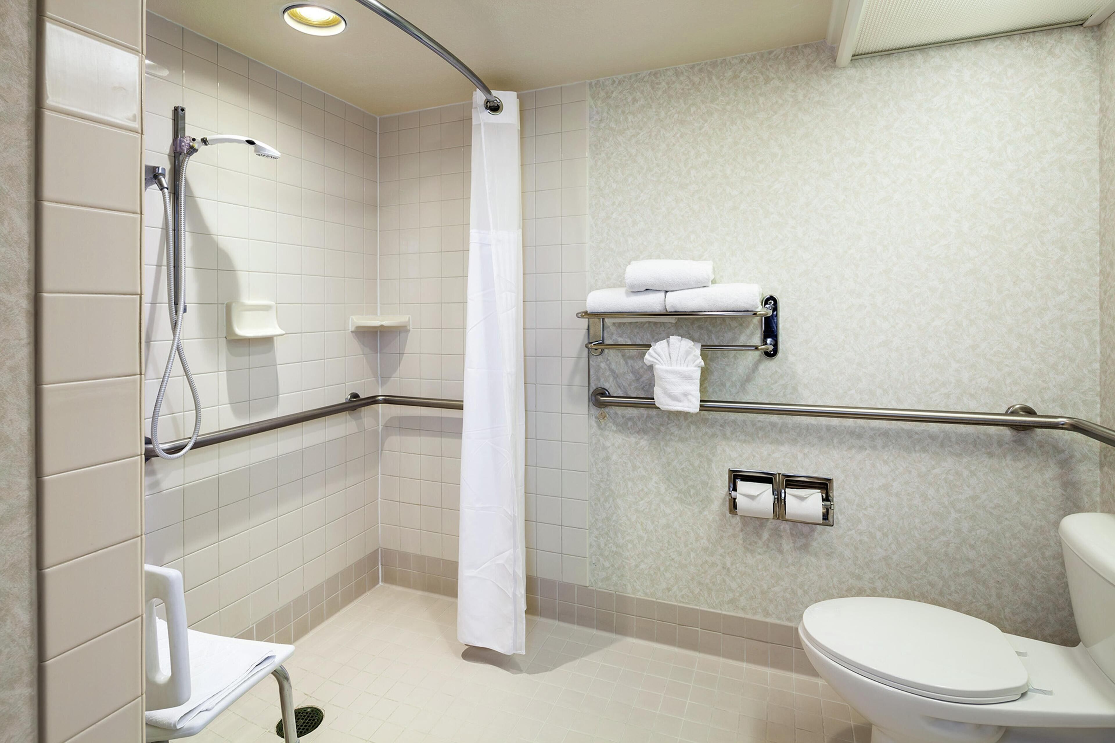 Un baño con ducha, inodoro y barras de apoyo.