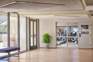 Un interior moderno con un banco, una planta en maceta y una puerta que da a una zona de gimnasio.