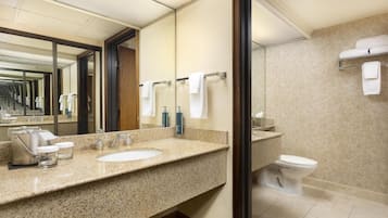 A hotel bathroom with a granite countertop sink, a mirror, a toilet, and a towel rack.