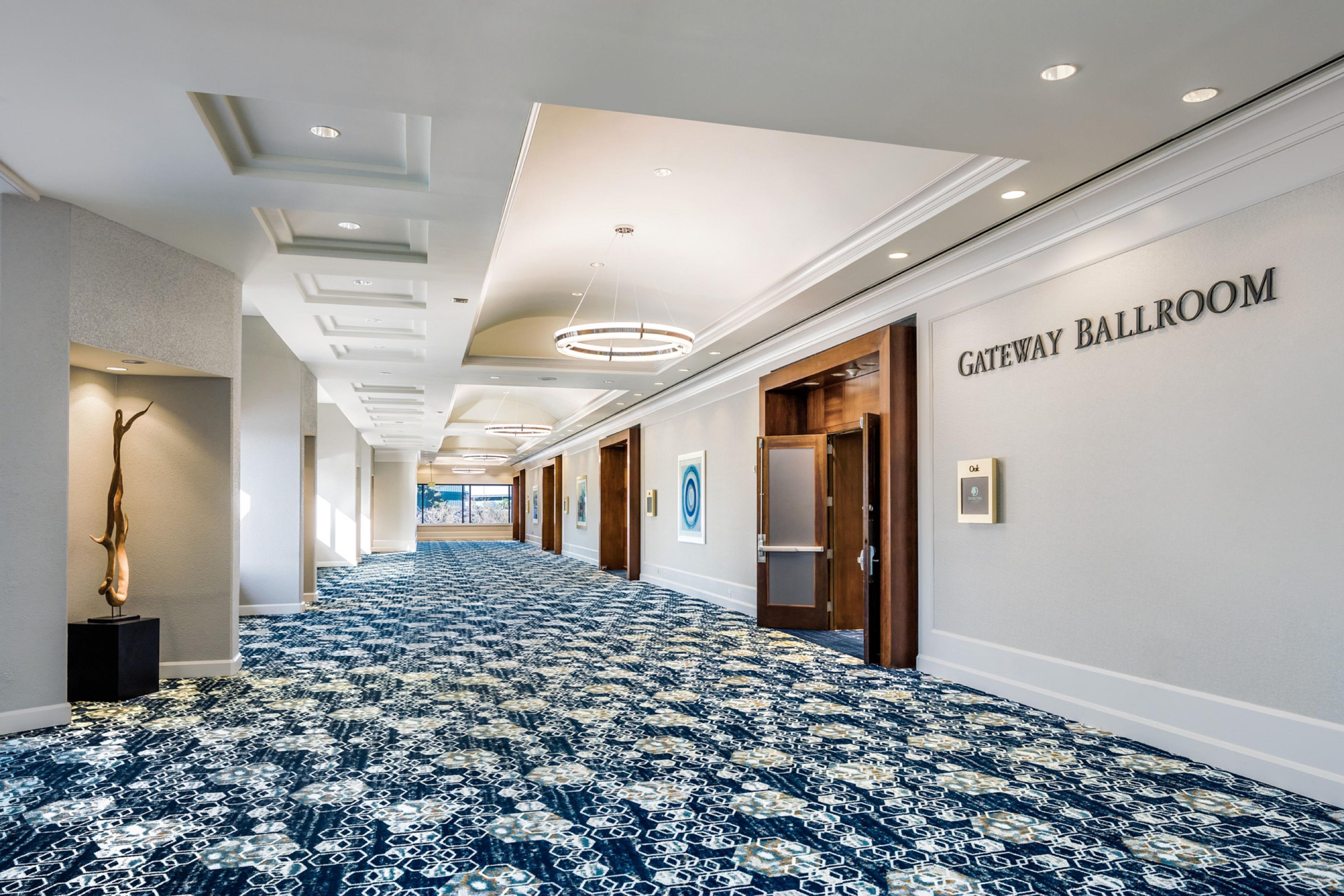 A hotel corridor with a patterned carpet, a wall sign reading 'GATEWAY BALLROOM', and a sculpture on the left.