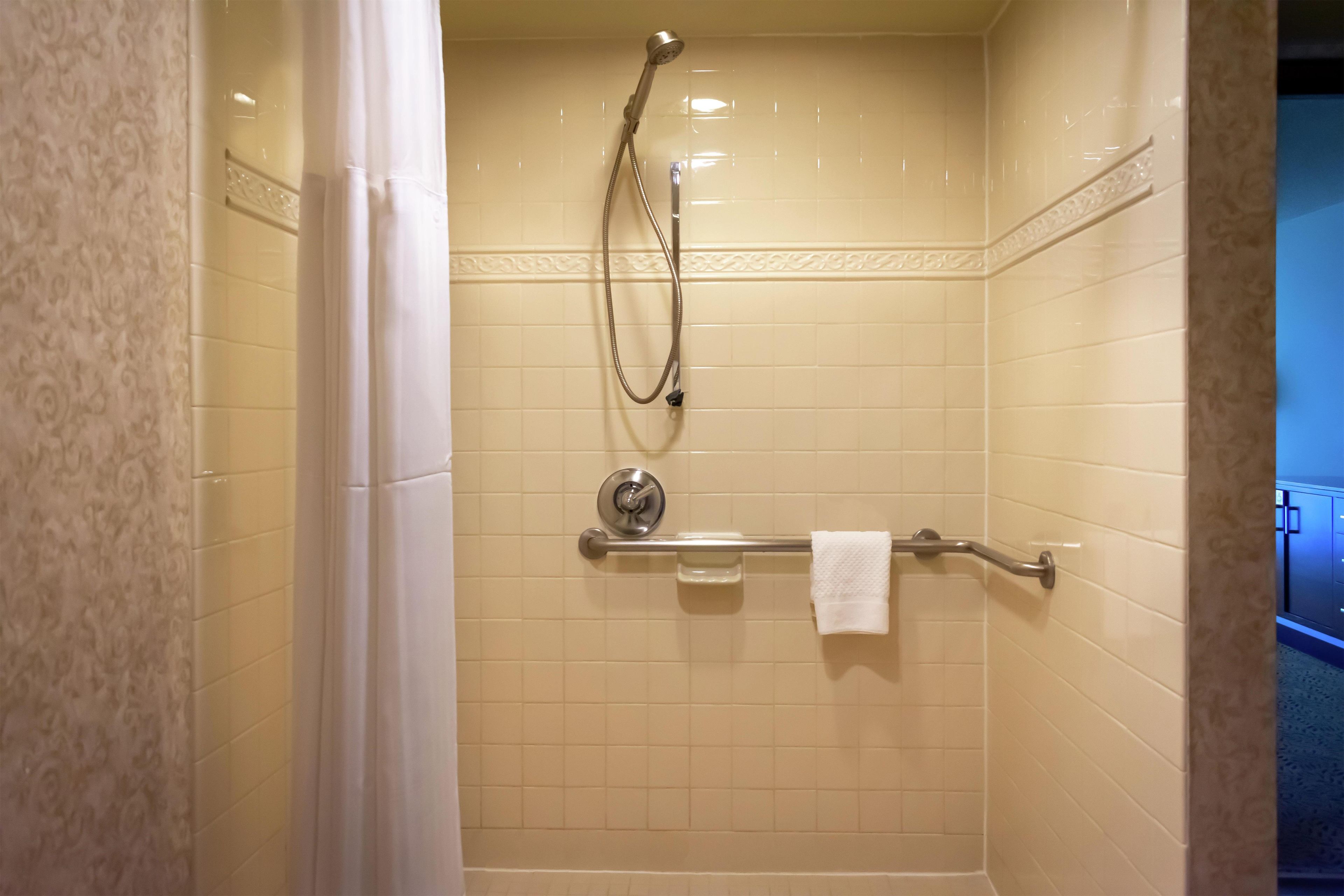 A shower with a handheld showerhead, a towel rack, and a glass container.