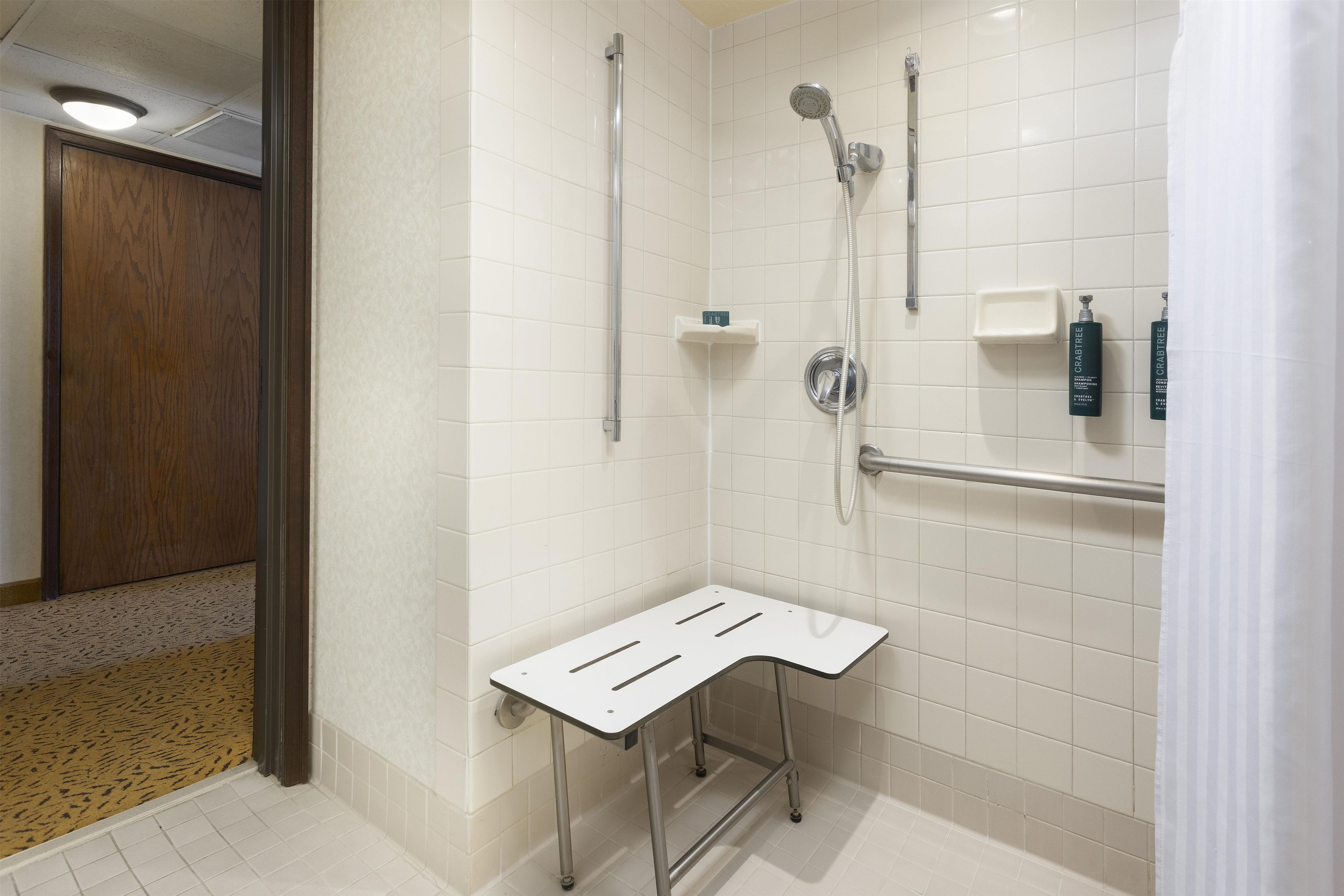Un espace douche moderne équipé d’une barre d’appui, d’un pommeau de douche à main et d’un robinet mural.