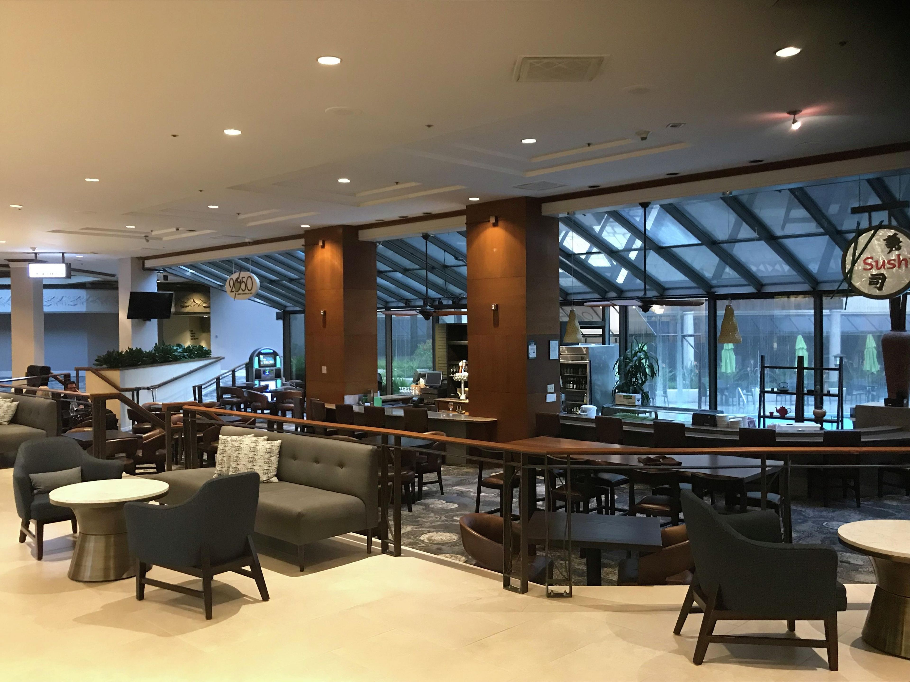 Un moderno vestíbulo de hotel con zonas de estar, un bar y un restaurante de sushi.