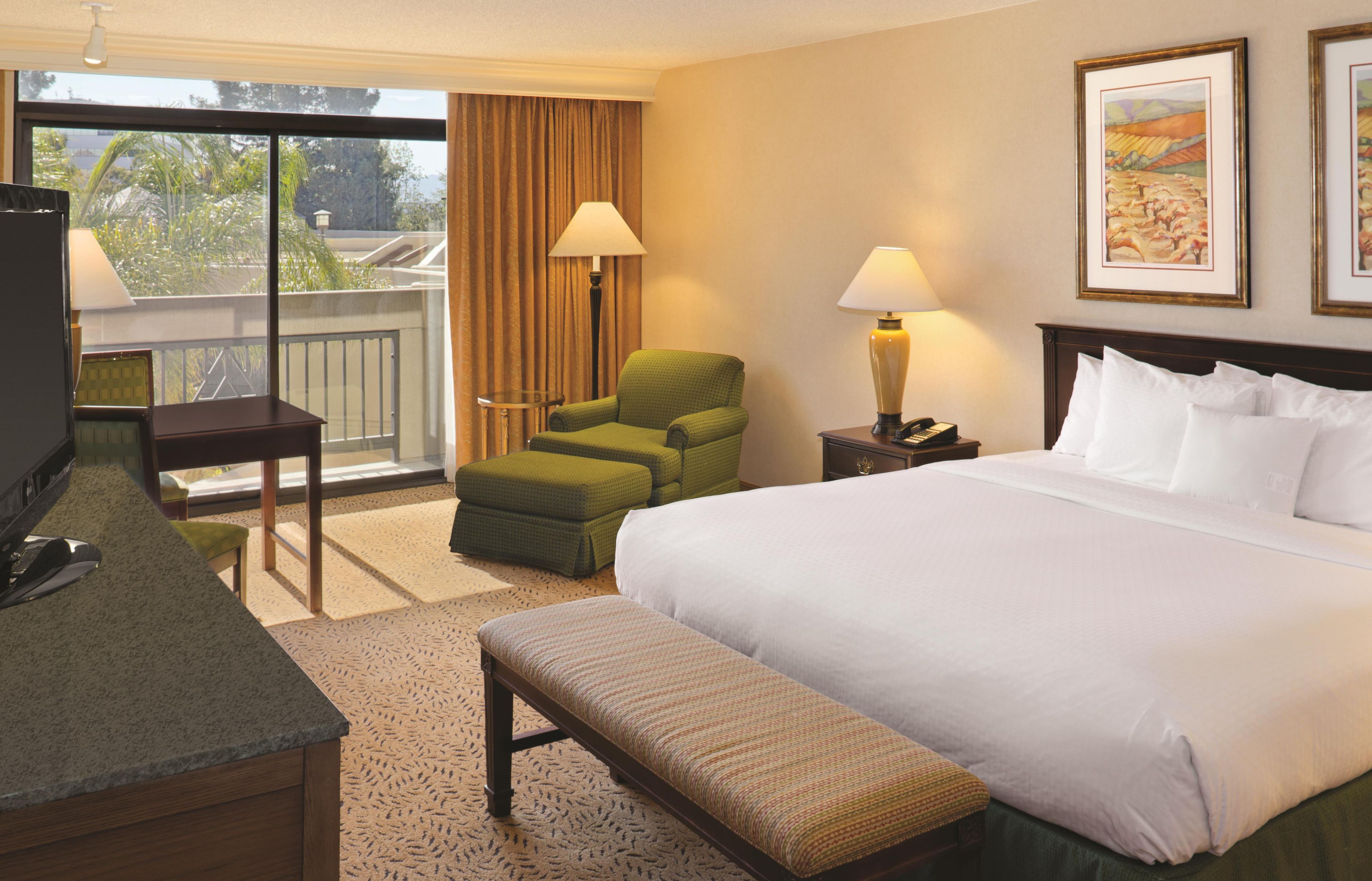 A hotel room with a bed, a chair, a desk, a lamp, and a painting on the wall.