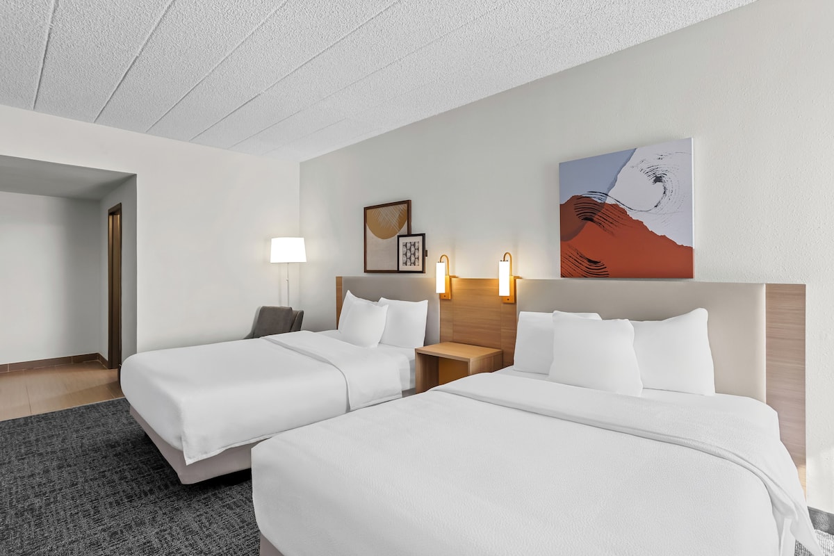 Une chambre d’hôtel avec deux lits, une table de chevet, une lampe et une œuvre d’art murale.