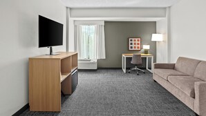 A hotel room with a flat-screen TV, a desk with a lamp, a sofa, and a window with curtains.