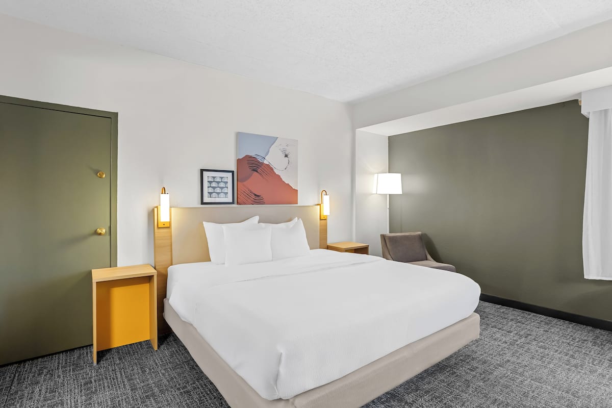 Une chambre d’hôtel avec un grand lit, deux tables de chevet, une petite table, une chaise et un tableau au mur.