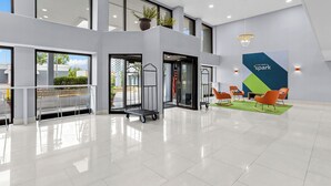 A spacious lobby with a clean, modern design, featuring a large seating area with orange chairs, a service cart, and a prominent 'Spark' sign on the wall.