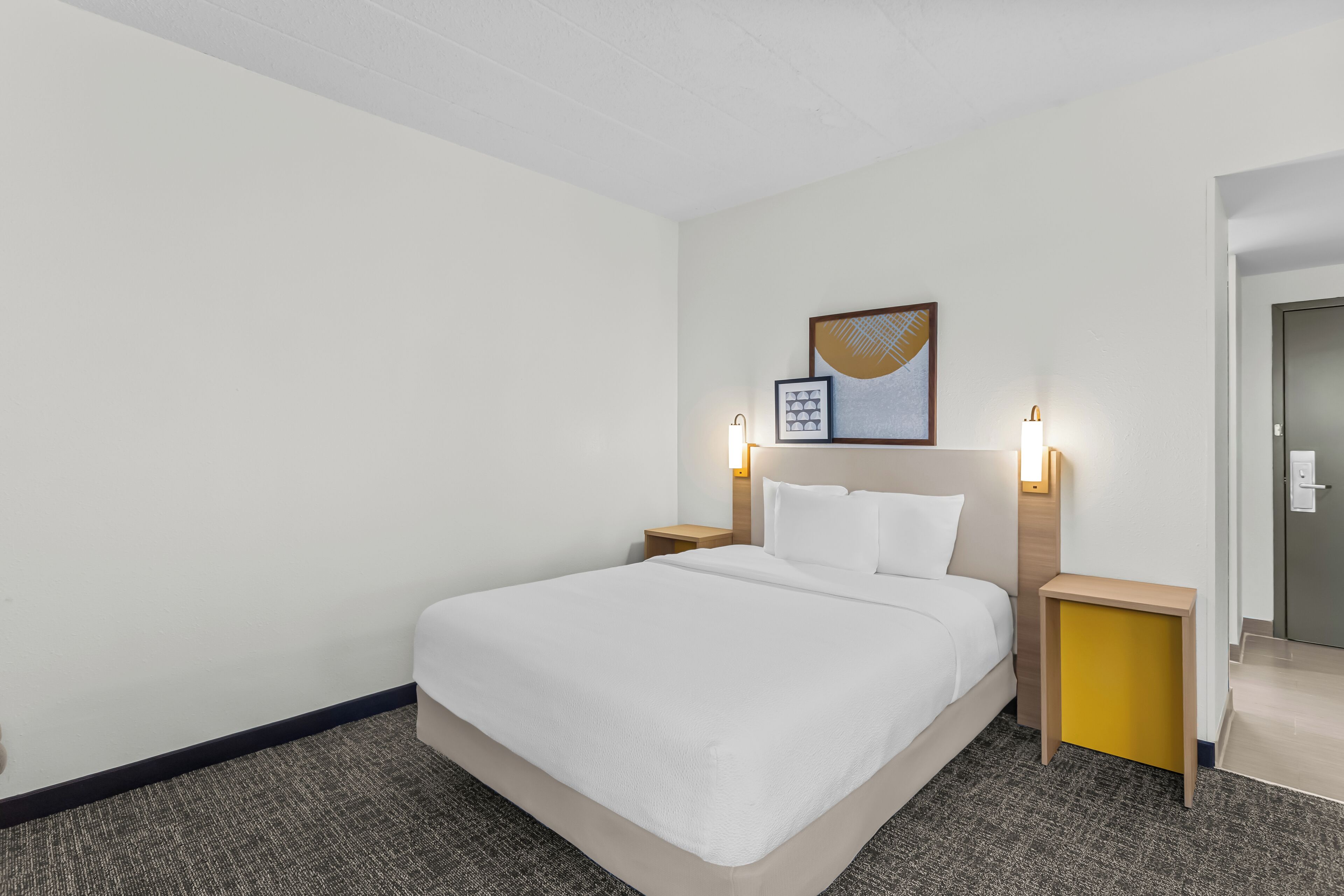 A hotel room with a large bed, two bedside tables, a headboard with a light, and a framed picture on the wall.