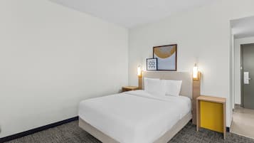 A hotel room with a large bed, two bedside tables, a headboard with a light, and a framed picture on the wall.