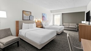A hotel room with two beds, a sofa, a desk, and a TV.
