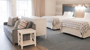 A hotel room with two beds, a sofa, a small table, and a window with curtains. - Howard Johnson by Wyndham Middletown Newport Area (Middletown)