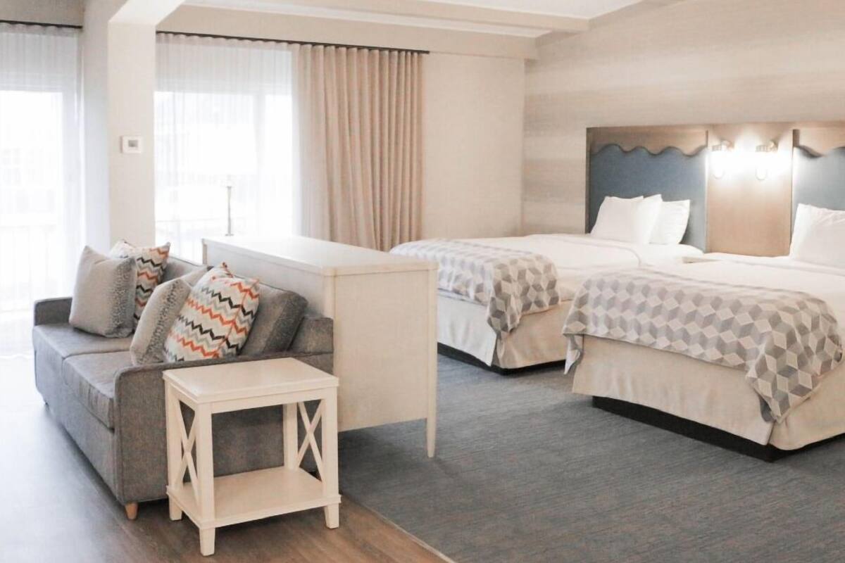 A hotel room with two beds, a sofa, a small table, and a window with curtains.