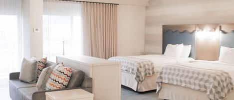 Habitación de hotel con dos camas, un sofá, una mesita y una ventana con cortinas.