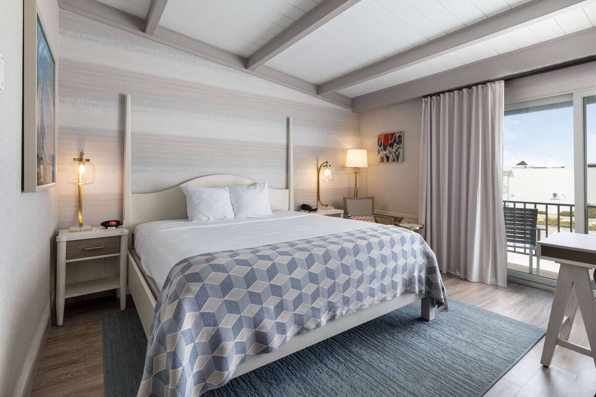 A hotel room with a bed, bedside tables, a desk, and a balcony with curtains.