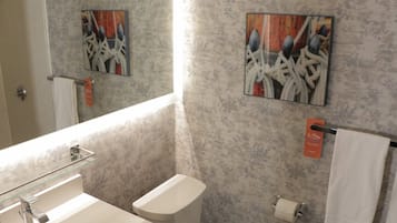 Un baño con pared de mármol, un lavamanos de cristal, un inodoro y dos cuadros abstractos.
