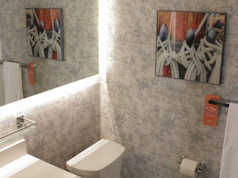 Un baño con pared de mármol, un lavamanos de cristal, un inodoro y dos cuadros abstractos.