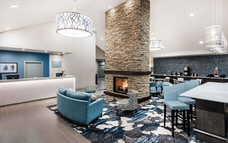 A modern hotel lobby with a stone fireplace, blue seating, and a bar area.