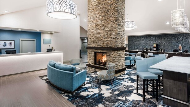 A modern hotel lobby with a stone fireplace, blue seating, and a bar area. - Howard Johnson by Wyndham Middletown Newport Area (Middletown)