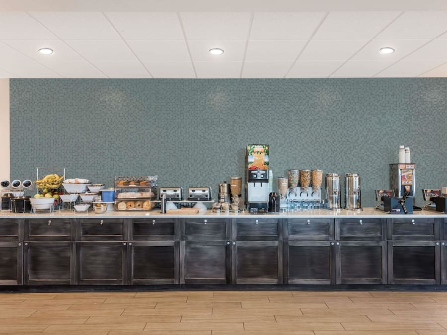 A breakfast bar with various food items and beverages, a coffee machine, and storage cabinets.